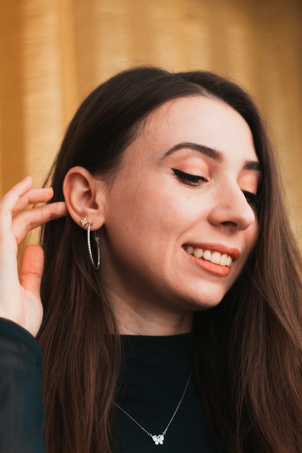 Woman touching her silver earring while wearing a butterfly necklace.