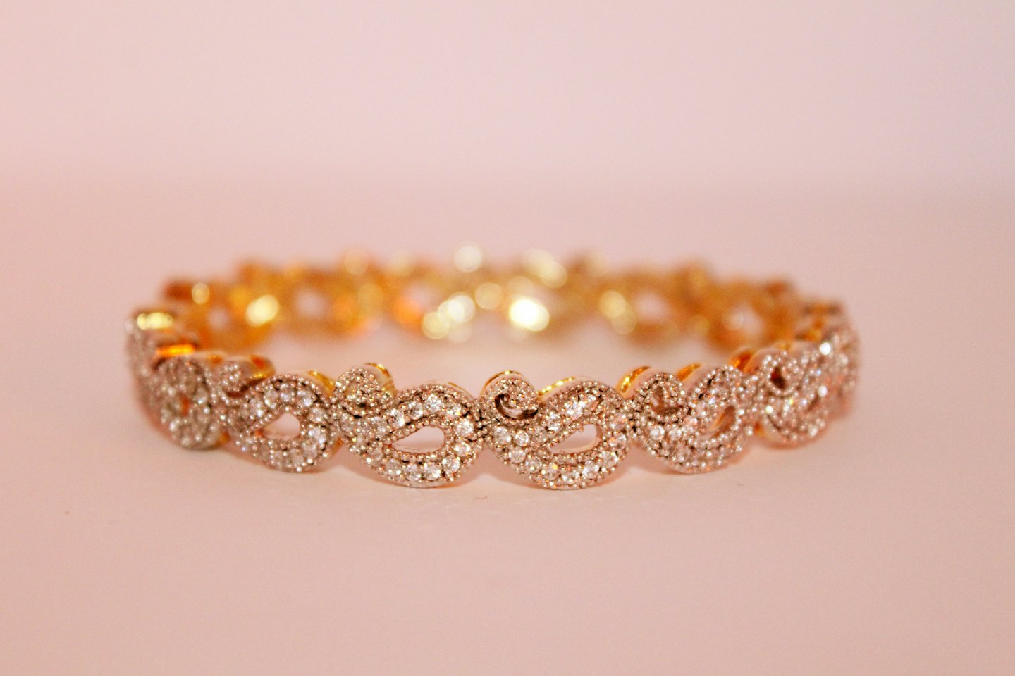 Sparkling gold bracelet with intricate pattern on pink surface.