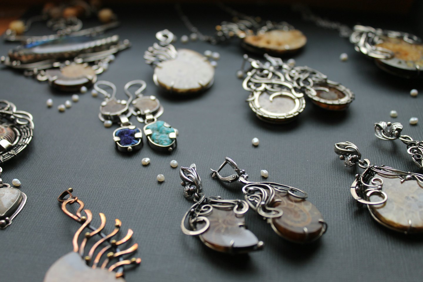 Artisanal wire-wrapped jewelry with natural stones and pearls arranged on stone.