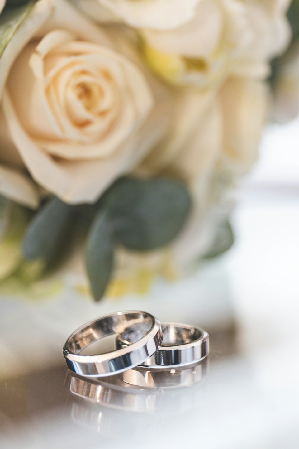 Two silver wedding rings rest on a reflective surface.
